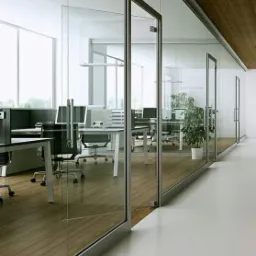 Nowoczesne biuro z przeszklonymi ścianami działowymi i drewnianą podłogą, widok na stanowiska pracy z komputerami i krzesłami biurowymi.