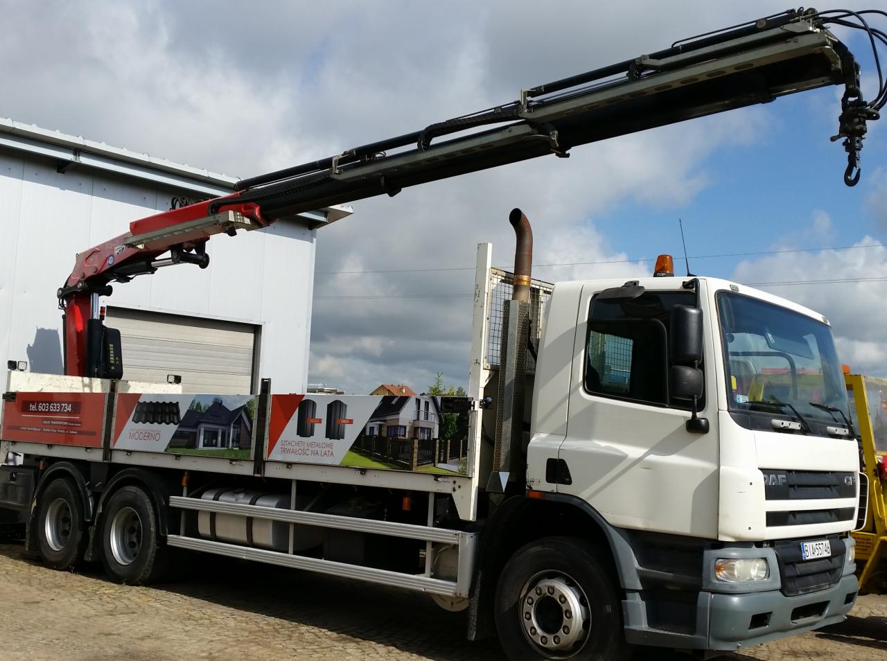 Ciężarówka z dźwigiem hydraulicznym, na boku reklama metalowych dachów i elewacji budynków.