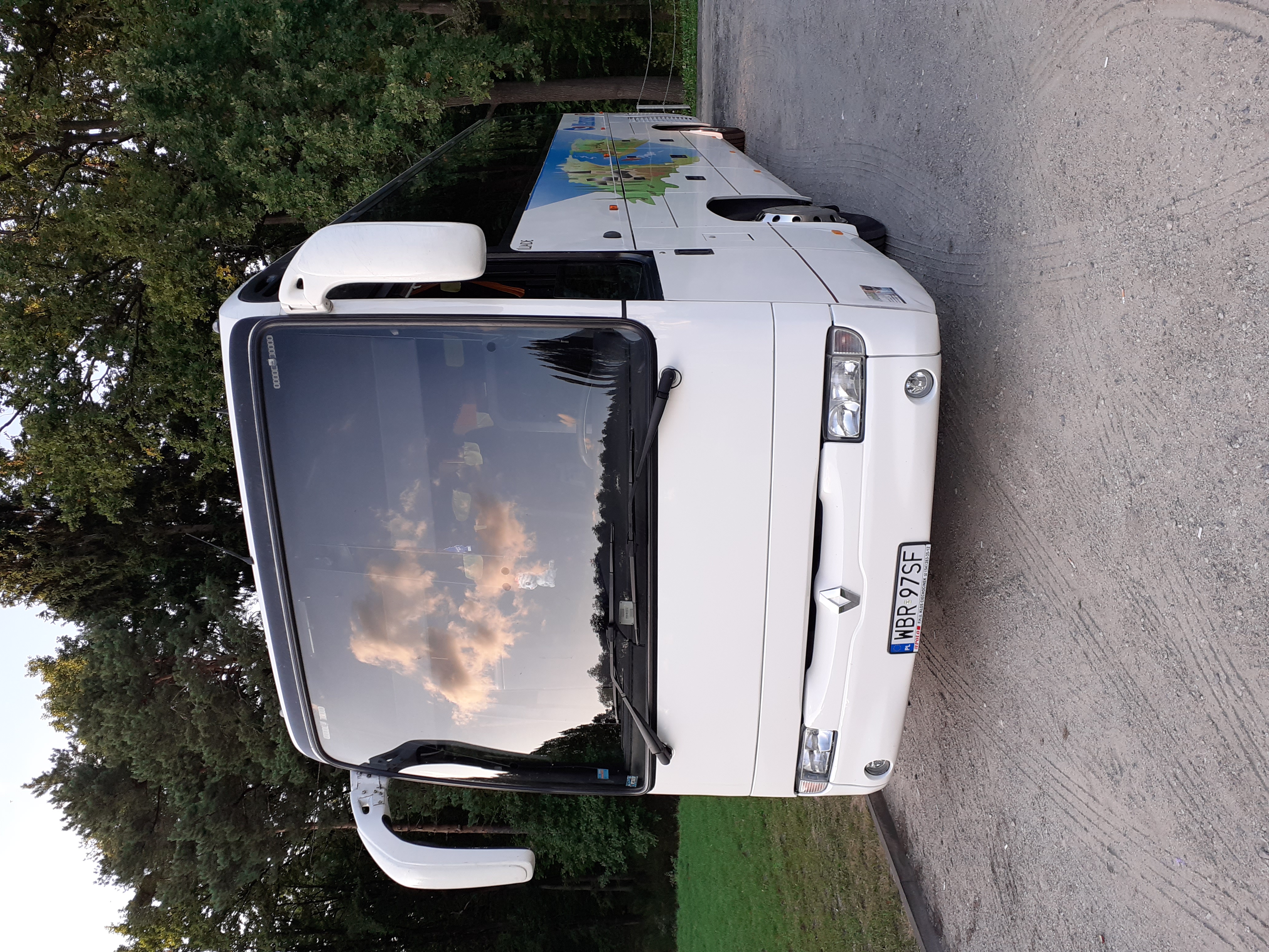 Przód białego autobusu z polską tablicą rejestracyjną WBR 97SF, zaparkowanego na parkingu z widocznym odbiciem chmur w przedniej szybie.