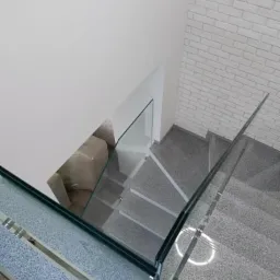 Schody wykończone szarym kamieniem z balustradą ze szkła hartowanego, widok z góry, ściana z białej cegły w tle.