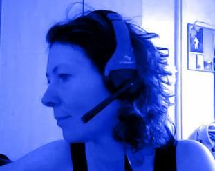 Portret kobiety z krótkimi, ciemnymi włosami i zestawem słuchawkowym na głowie, profil z lewej strony, niebieska tonacja zdjęcia.