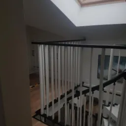 Nowoczesne schody z biało-czarną balustradą z pionowych prętów, widok z góry, okno dachowe w tle.