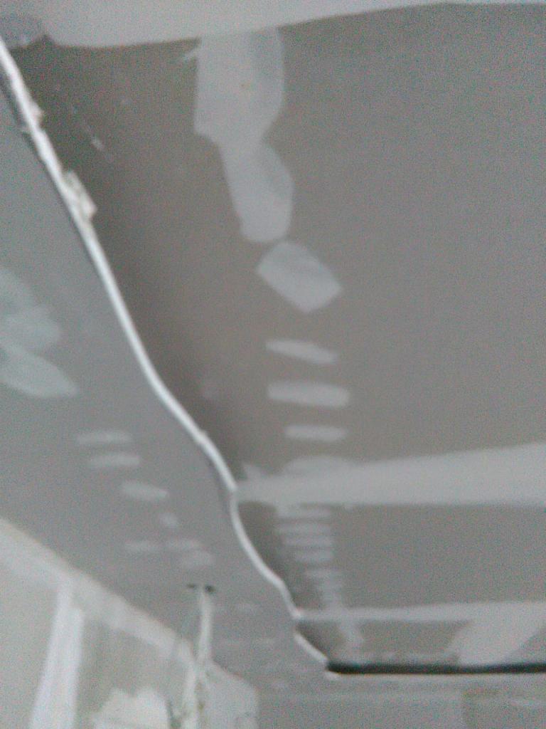 Niedokończona gładź na suficie z widocznymi łatami i niedoskonałościami, przygotowana do szlifowania.