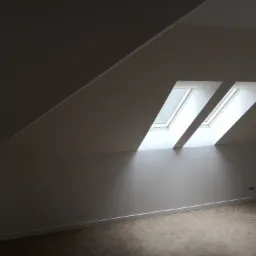 Poddasze po remoncie z dwoma oknami dachowymi wpuszczającymi światło, jasne ściany i podłoga ułożona w jodełkę.