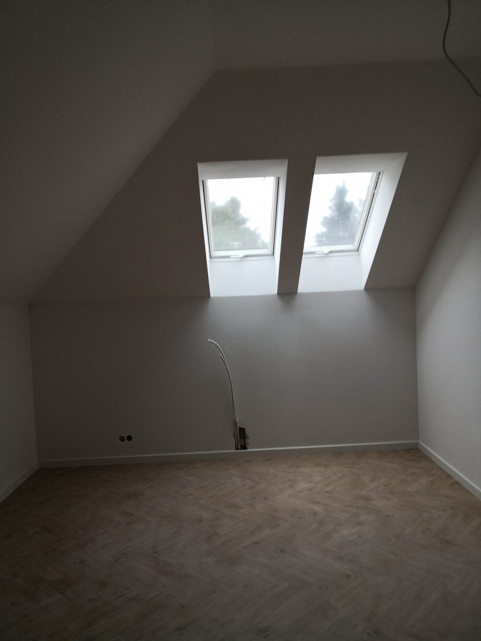 Poddasze po remoncie z dwoma oknami dachowymi i parkietem ułożonym w jodełkę, widoczne kable wystające ze ściany.