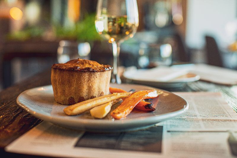 Pieczeń w cieście na talerzu z warzywami i kieliszkiem białego wina na tle restauracji.