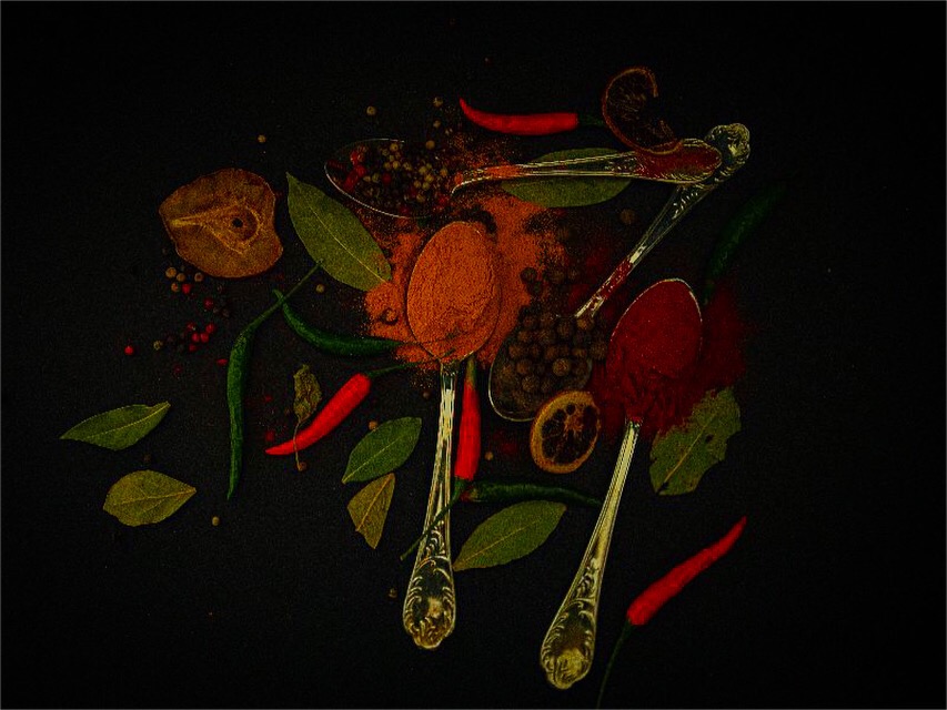 Kompozycja z przypraw: papryka czerwona i zielona, ziarna pieprzu, liście laurowe, suszona skórka pomarańczy i łyżki z przyprawami na ciemnym tle.