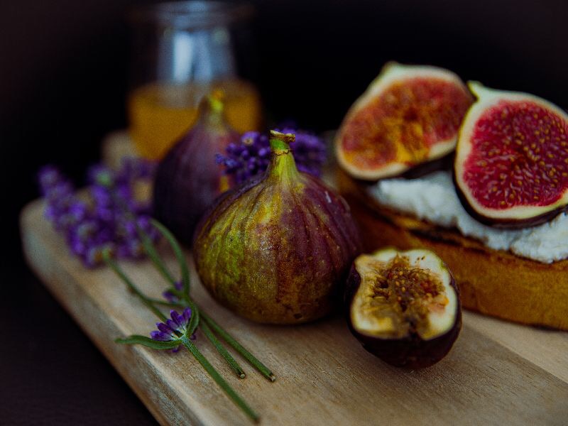 Kompozycja z fig, lawendy, miodu i grzanki z kremowym serem na drewnianej desce, w ciepłym oświetleniu.