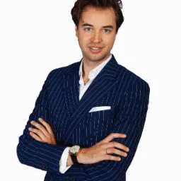 Młody mężczyzna w eleganckim, dwurzędowym garniturze w prążki, z zegarkiem na ręku, pozuje na białym tle, prezentując profesjonalny wizerunek.