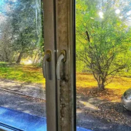 Okna w Katowicach: Połowa szyby umyta, druga brudna, widoczne zacieki i zabrudzenia na ramie okiennej, za oknem jesienny park.