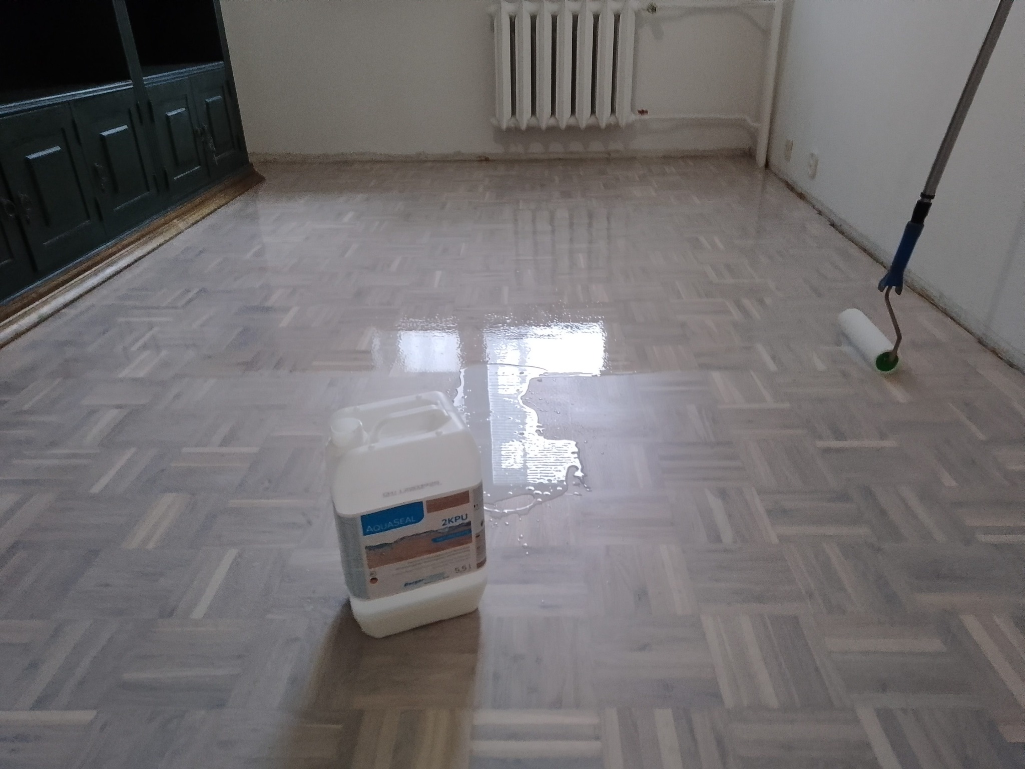 Parkiet po nałożeniu lakieru, widoczny wałek malarski i pojemnik z lakierem Aquaseal 2KPU.