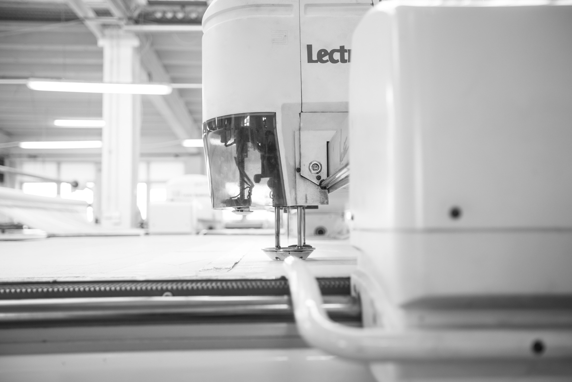 Automatyczna krajalnica Lectra w szwalni, precyzyjnie tnąca materiał. Widoczne detale maszyny i proces cięcia. Czarno-biała fotografia podkreśla techniczną naturę.