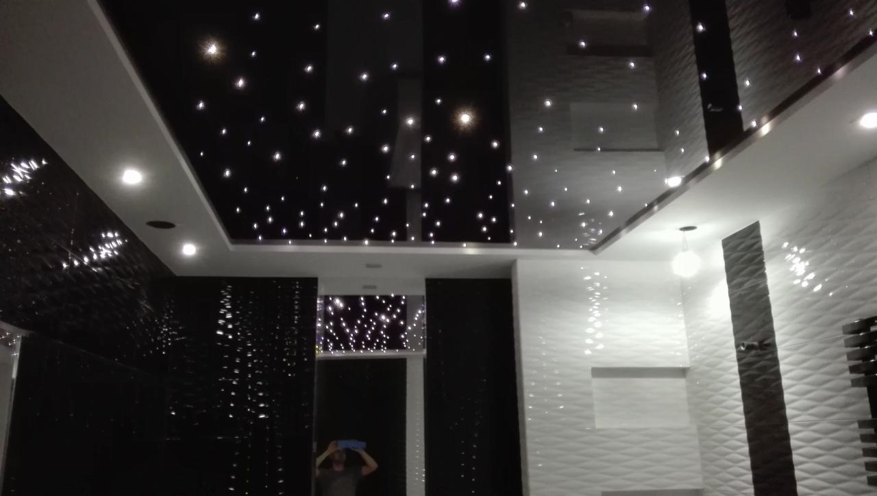 Błyszczący sufit z efektem gwiazd i czarno-białe ściany z teksturą w nowoczesnym wnętrzu, widoczna osoba w tle.