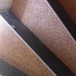 Wykończone schody z żywicy epoksydowej w odcieniach brązu, z ciemnymi, metalowymi listwami antypoślizgowymi. Widok z g&oacute;ry, jasne oświetlenie, drobna faktura żywicy.