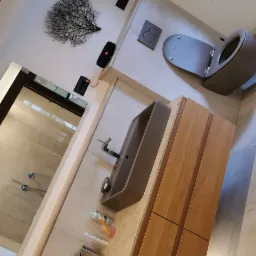 Nowoczesna łazienka z szarą ceramiką, drewnianą szafką pod umywalką, kabiną prysznicową typu walk-in i oknem dachowym z białą firanką.