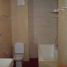 Wykończona łazienka w beżowych płytkach z widoczną toaletą, wanną i umywalką, wyposażona w chromowane akcesoria łazienkowe.