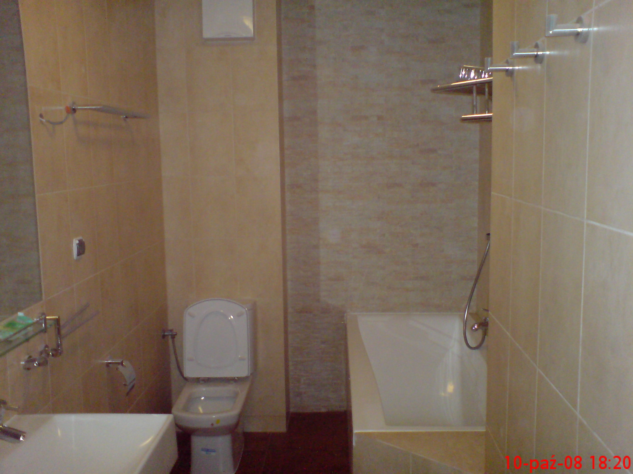 Wykończona łazienka w beżowych płytkach z widoczną toaletą, wanną i umywalką, wyposażona w chromowane akcesoria łazienkowe.