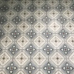 Wzór podłogi z płytek ceramicznych w odcieniach szarości i beżu, z motywem kwiatowym i geometrycznym, ułożonych w regularny deseń.