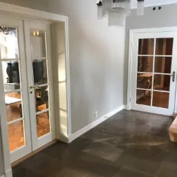 Wnętrze z ciemną, marmurkową posadzką z płytek w dużym formacie, widoczne białe, przeszklone drzwi i designerski żyrandol z kryształkami.