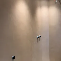 Beżowa ściana w rogu pomieszczenia z widocznymi otworami instalacyjnymi i punktowym oświetleniem sufitowym