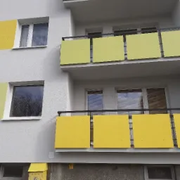 Odnowiona elewacja bloku z balkonami, z panelami w odcieniach żółci i limonki, widoczne skrzynki pocztowe w dolnej części budynku.