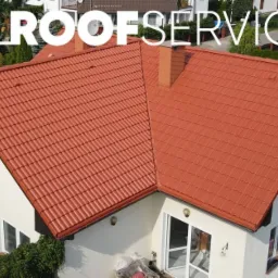 Czerwony dach z dachówki ceramicznej po renowacji w Elblągu, widok z góry na dom z białymi ścianami i kwiatami w oknach.