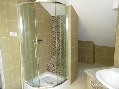 Kabina prysznicowa narożna z półokrągłymi drzwiami w łazience na poddaszu, wykończonej brązowymi płytkami ceramicznymi i mozaiką w strefie prysznica.