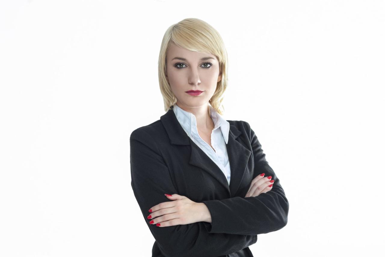 Portret kobiety w czarnym żakiecie i białej koszuli, skrzyżowane ręce, czerwone paznokcie, jasne włosy, na jasnym tle. Profesjonalny wizerunek.