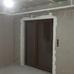 Wnętrze w trakcie remontu w Strzeszowie: widoczne płyty kartonowo-gipsowe na ścianach i suficie, przygotowane otwory na gniazdka elektryczne oraz wyprowadzone przewody oświetleniowe, czekające...