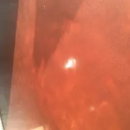 Błyszcząca, pomarańczowa powierzchnia podłogi z widocznym odbiciem światła i fragmentem szarej ściany przy krawędzi.