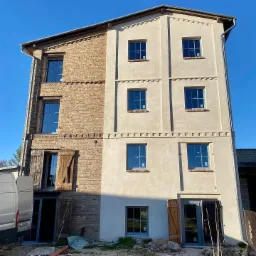 Odrestaurowany budynek z częściowo odsłoniętą cegłą i nowymi oknami, z widocznym fragmentem samochodu dostawczego po lewej stronie.