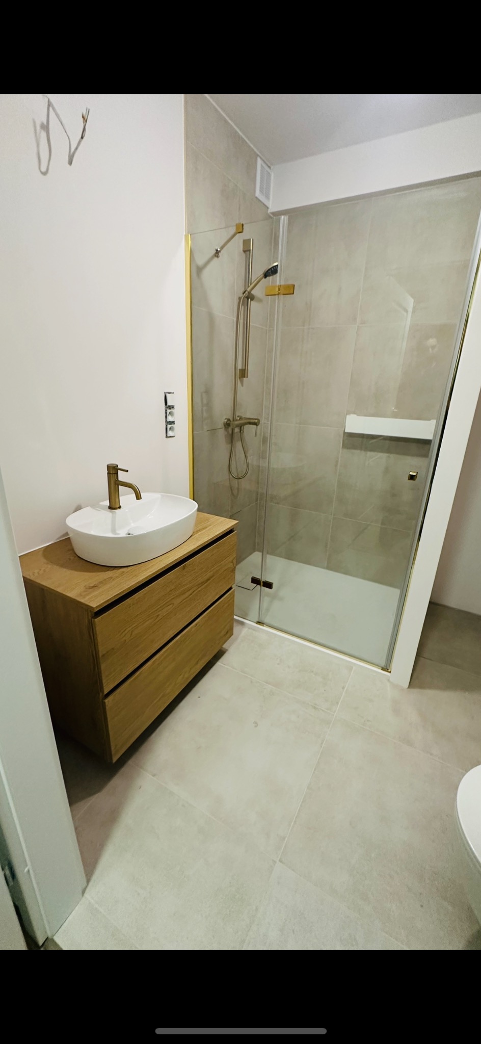 Nowoczesna łazienka z kabiną prysznicową w odcieniach szarości i beżu. Umywalka nablatowa na drewnianej szafce z złotą armaturą. Minimalistyczny design.