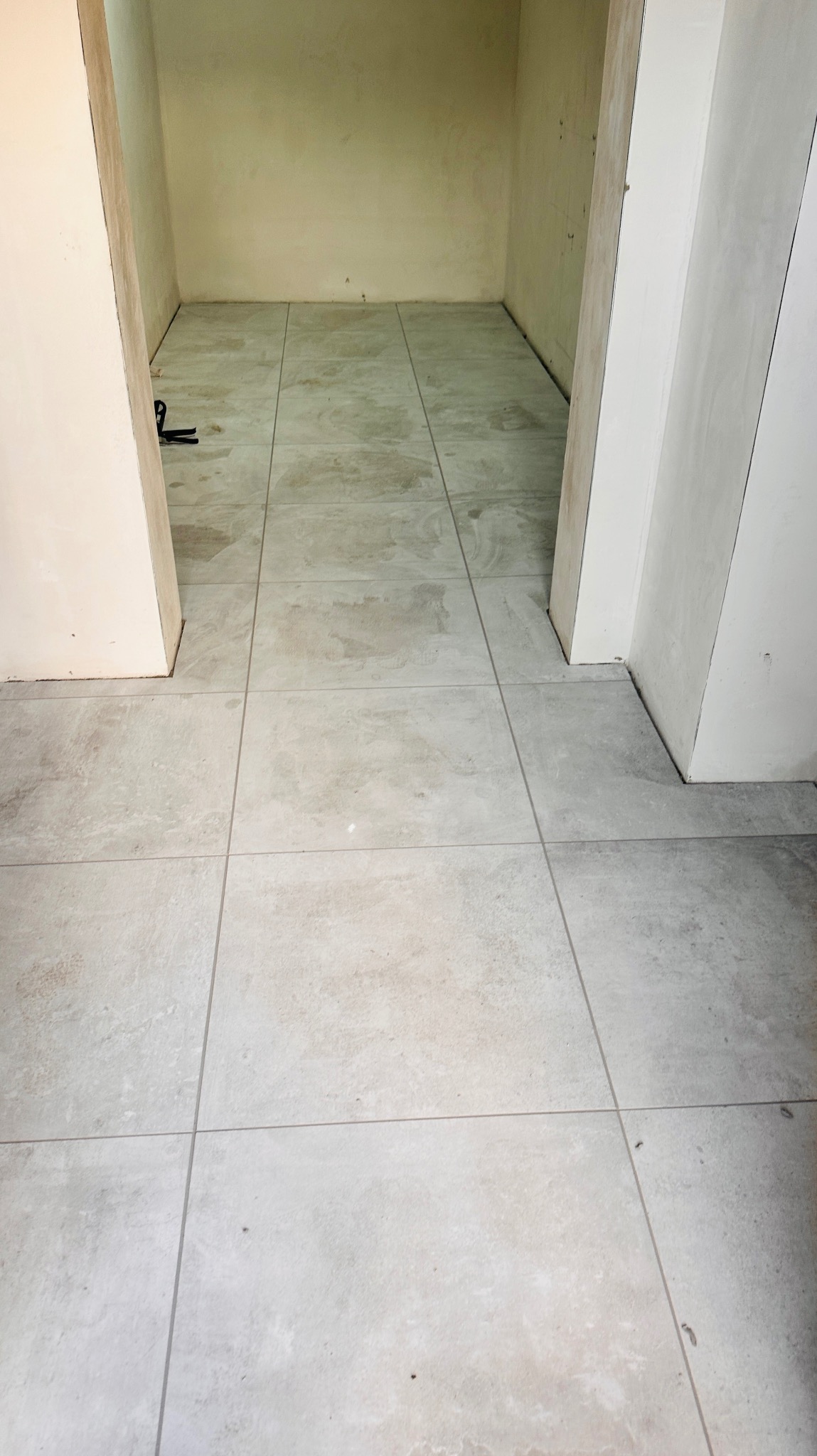 Ułożone, jasne płytki podłogowe w pomieszczeniu w trakcie wykańczania wnętrza. Prace glazurnicze w Poznań. Widoczne narzędzia.