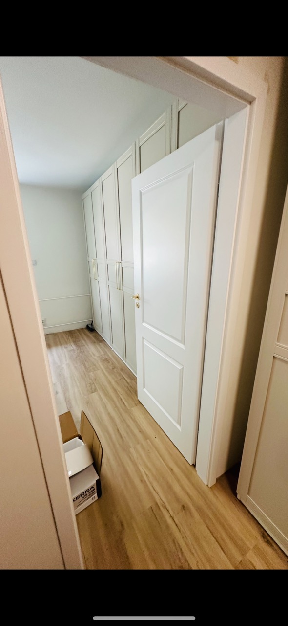 Białe drzwi wewnętrzne z ościeżnicą, zamontowane w pokoju z panelami podłogowymi i zabudową szafy wnękowej. Widoczny fragment kartonu po panelach.