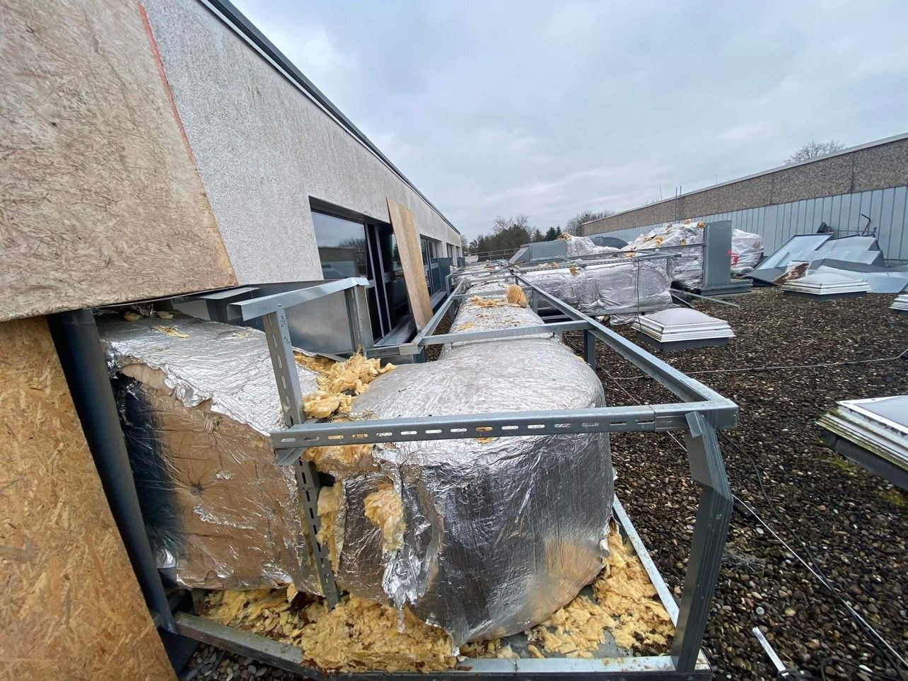 Demontaż izolacji z folii aluminiowej i wełny mineralnej na dachu budynku, widoczne elementy konstrukcyjne i gruz budowlany.