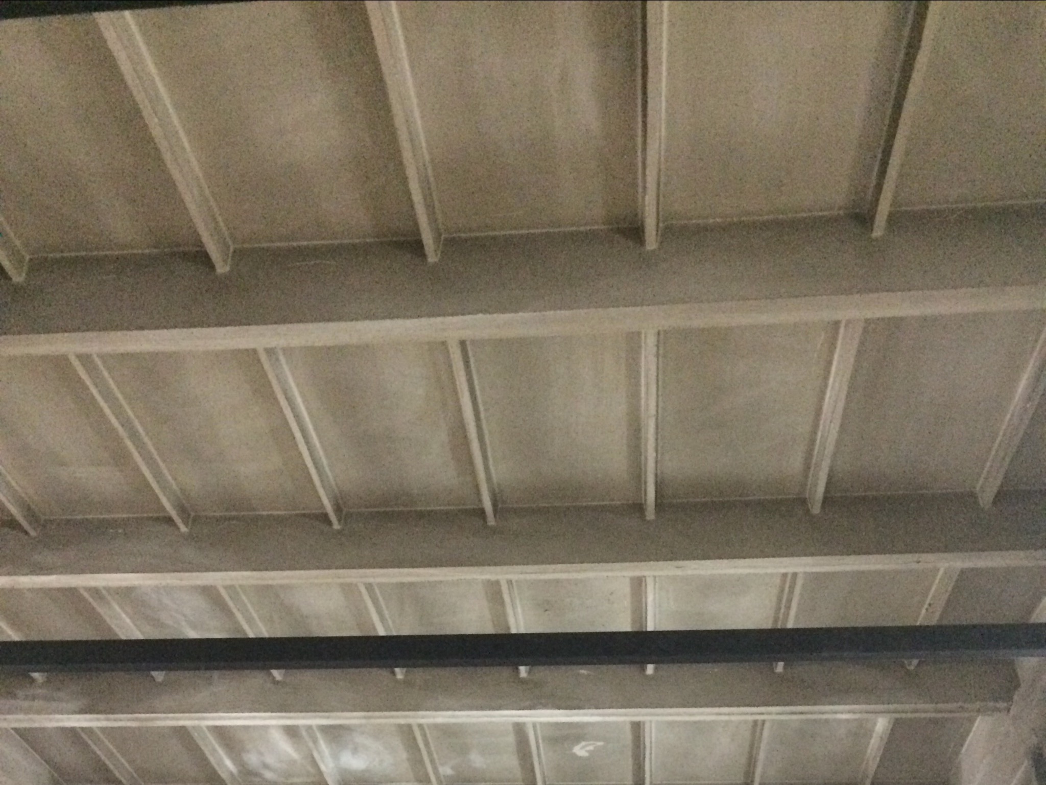 Szara, surowa konstrukcja sufitu z widocznymi belkami nośnymi, prawdopodobnie w trakcie prac wykończeniowych w Jeleniej Górze.