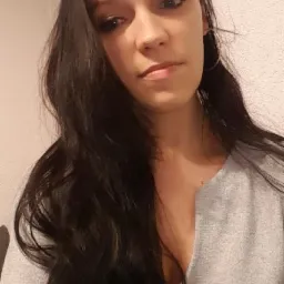 Portret kobiety w szarym swetrze z głębokim dekoltem. Długie, ciemne włosy opadają na ramiona. Delikatny makijaż, srebrne kolczyki. Ujęcie od dołu.