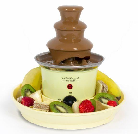 Fontanna czekoladowa z owocami (banany, kiwi, truskawki) i waflowymi ciasteczkami wokół podstawy, ustawiona na białym tle.