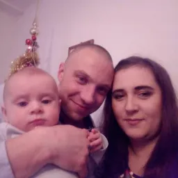 Zdjęcie rodziny z małym dzieckiem, z dekoracją świąteczną w tle, wykonane z bliskiej odległości.