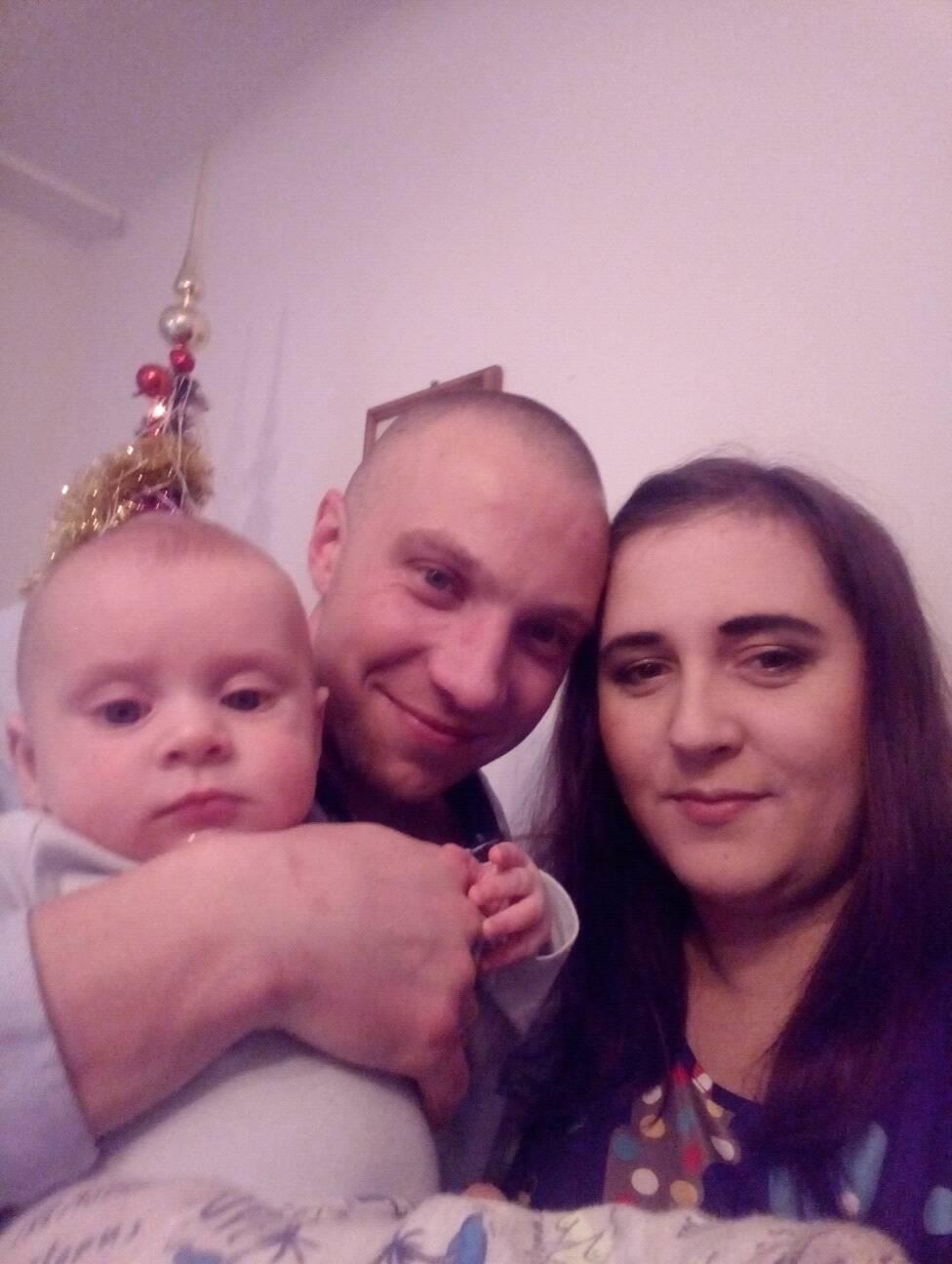 Zdjęcie rodziny z małym dzieckiem, z dekoracją świąteczną w tle, wykonane z bliskiej odległości.