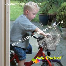 PPUH Sekret-foll - Chłopiec na rowerku uderza w okno zabezpieczone folią antywłamaniową, chroniącą przed rozbiciem. Widoczne pęknięcia na folii, ale szyba pozostaje cała.