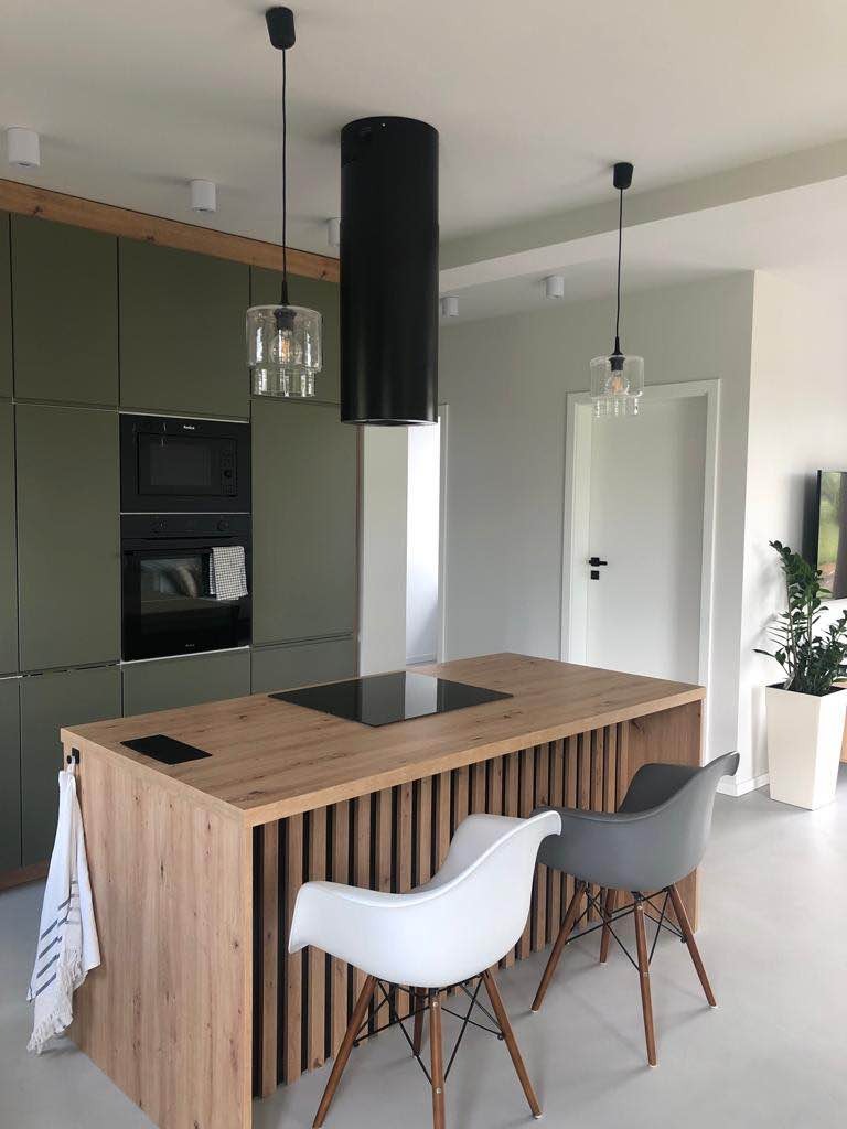 Nowoczesna kuchnia z wyspą wykończoną drewnem, czarnym okapem cylindrycznym i minimalistycznymi lampami wiszącymi, uzupełniona o designerskie krzesła Eames.
