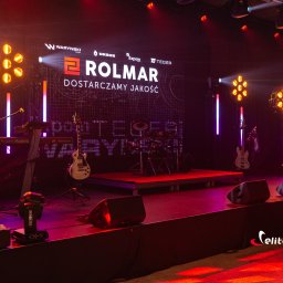 Elite Music Julian Dziewulski - Scena eventowa z instrumentami (gitara, perkusja, keyboard) i oświetleniem. Na tylnej ścianie logo firmy Rolmar. Widoczne głośniki i efekty świetlne.