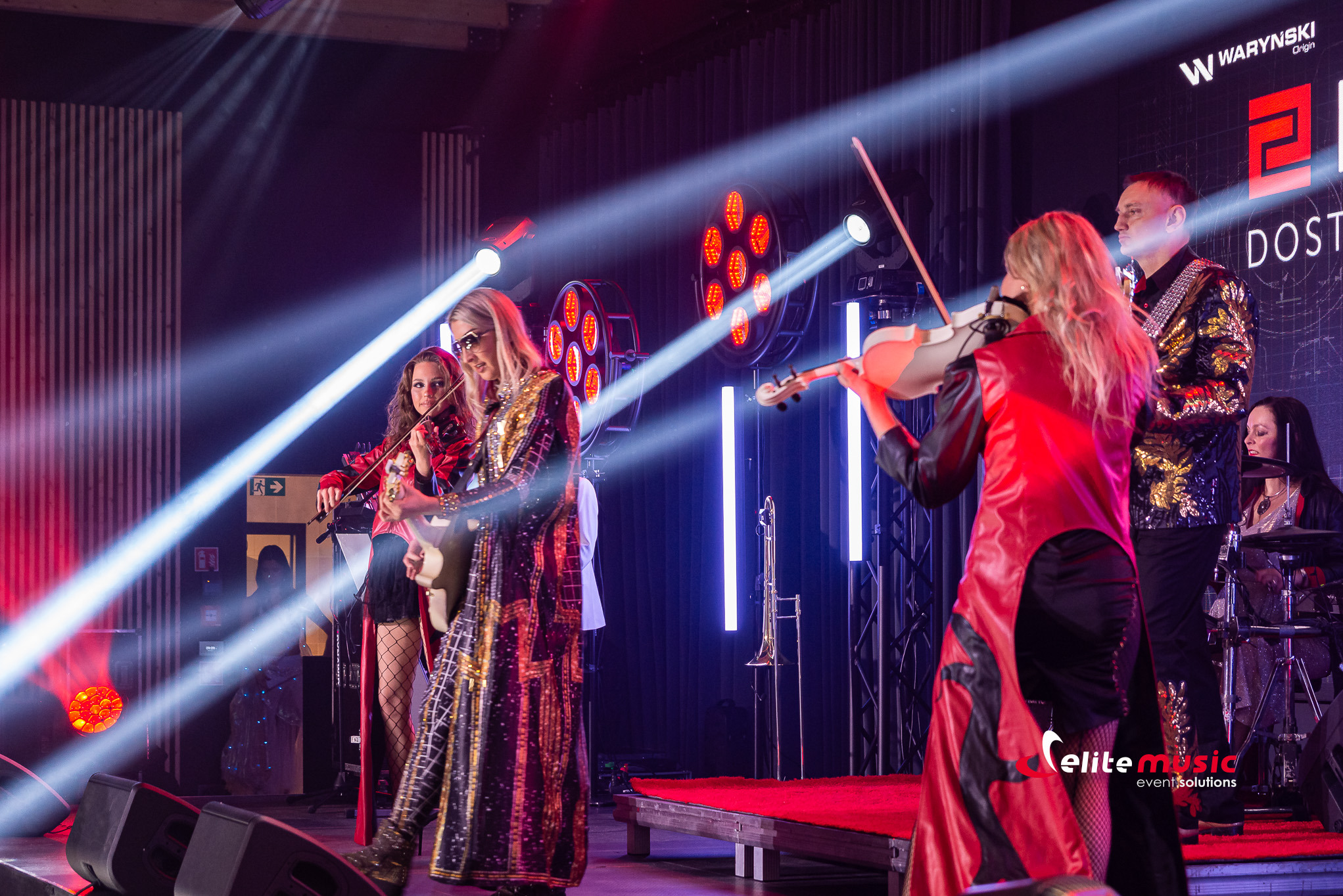 Zespół muzyczny na scenie z oświetleniem eventowym. Wokalistki grają na skrzypcach, perkusistka w tle. Koncert w Radisson Blu Sopot, realizacja Rolmar.