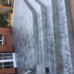 Betonowe schody zewnętrzne z efektem dekoracyjnym, przylegające do ceglanego budynku z oknami, widoczne ślady użytkowania.