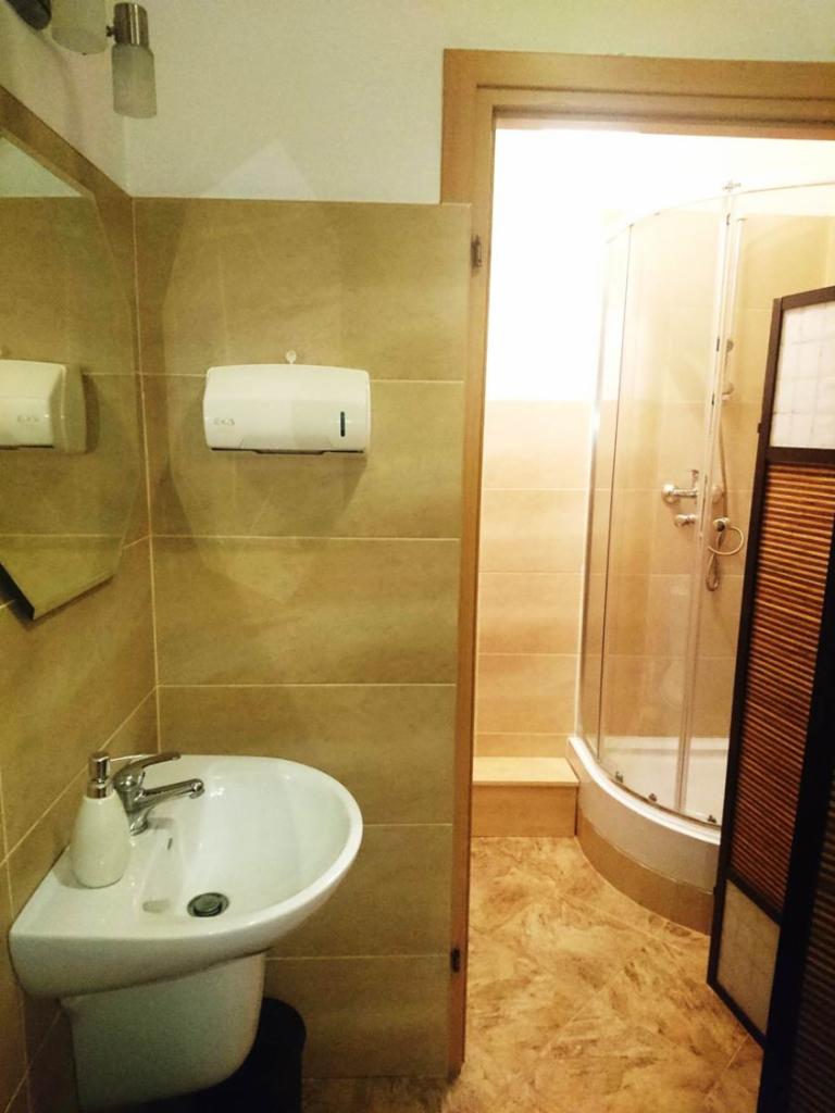 Jasna łazienka z umywalką, dozownikiem mydła i kabiną prysznicową z hydromasażem, wykończona beżowymi płytkami.