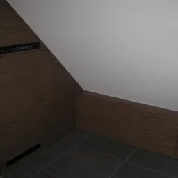 Zabudowa wnęki na poddaszu z drewnopodobnych paneli z ukrytymi otworami wentylacyjnymi, szara podłoga z płytek.