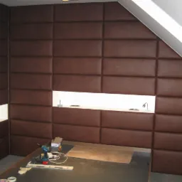 Montaż brązowych paneli tapicerowanych na ścianie w pokoju na poddaszu, widoczne narzędzia i oświetlenie LED w niszy.