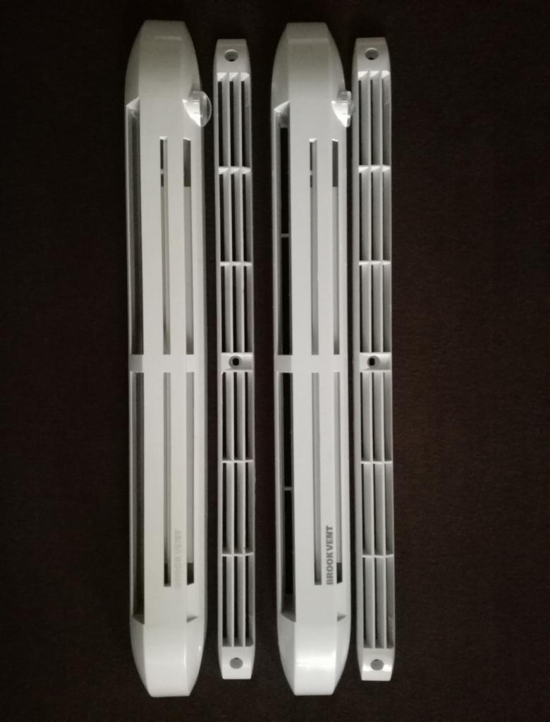 Cztery białe, podłużne kratki wentylacyjne Brookvent o różnej długości, ułożone na ciemnym tle, widoczne z bliska.