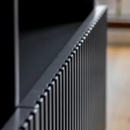 Fragment czarnej, nowoczesnej balustrady z pionowych listew, widok z bliska, z rozmytym tłem podłogi.